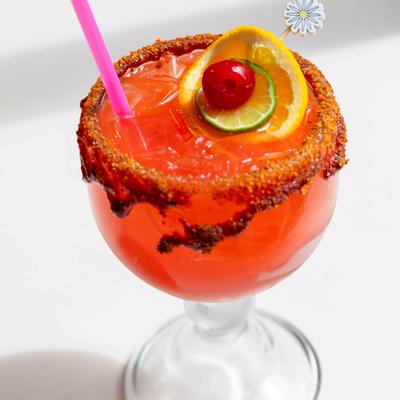 Chili-rimmed cocktail with cherry and citrus garnish.