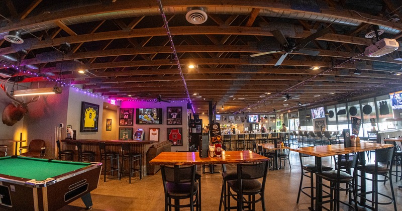 Interior of a bar, tables and chairs, pool table, wooden beams on the ceiling, purple lights