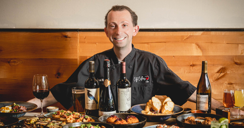 Smiling chef at a table with food and wine