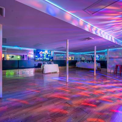 A spacious event room with a dance floor and colorful, projected lighting.