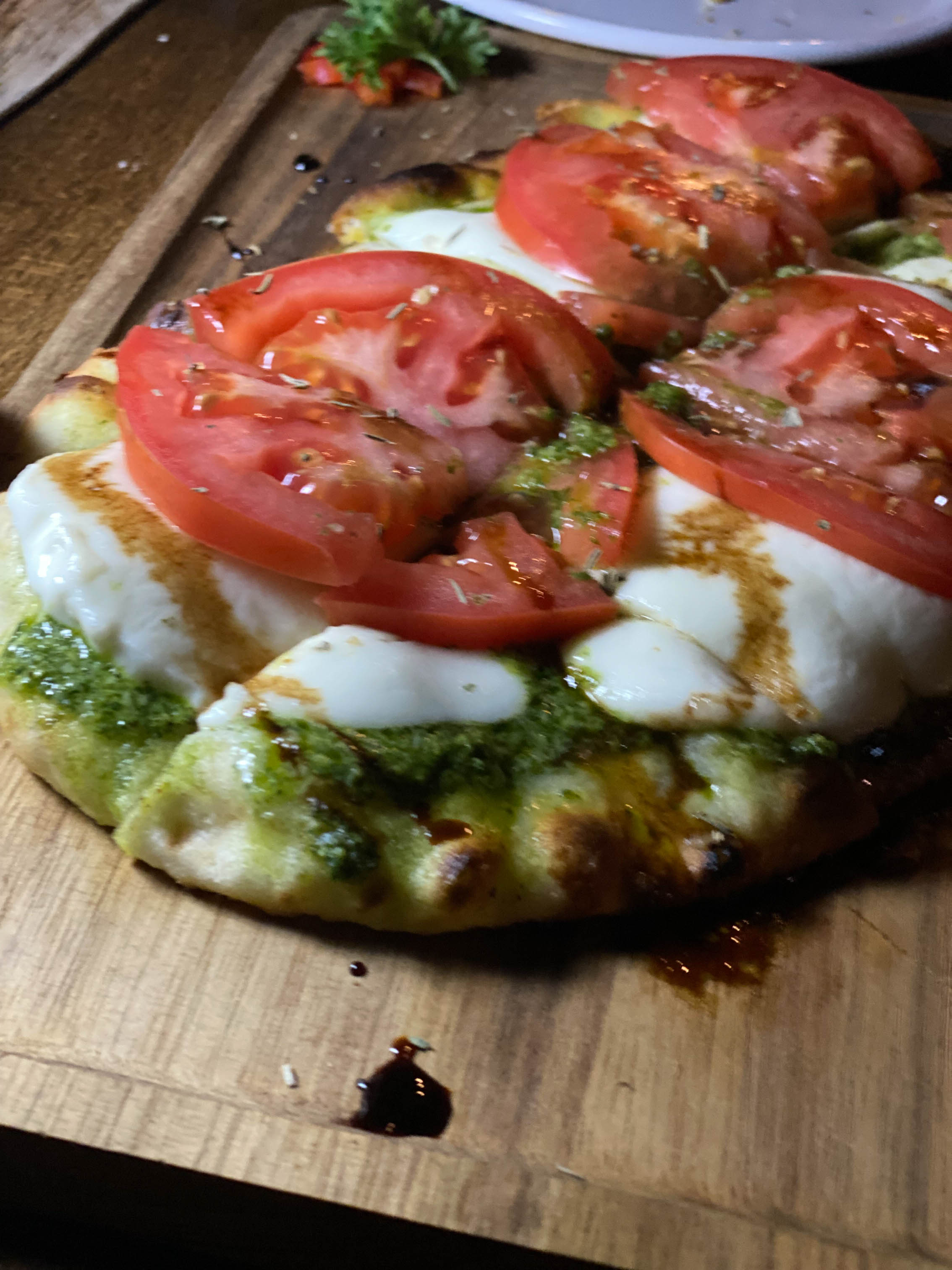 Margherita flatbread topped with pesto, cheese and tomatoes
