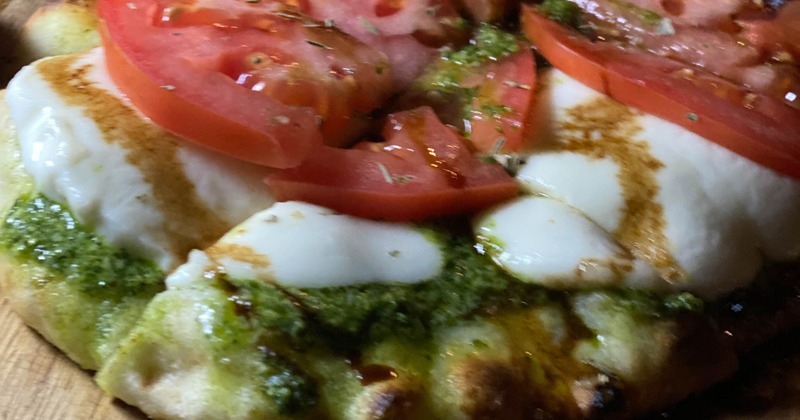 Margherita flatbread topped with pesto, cheese and tomatoes