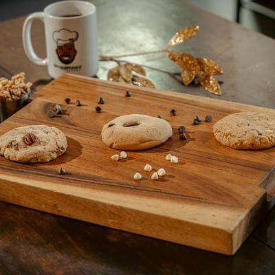 Three cookies on a wooden board with regular and white chocolate chips.
