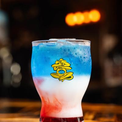 A colorful layered drink in a curvy glass, featuring red, white, and blue layers.