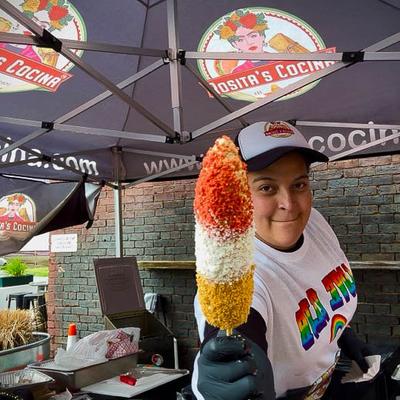 An employee holding a large corn on the cob in front of the camera.