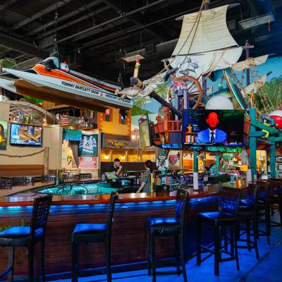 Vibrant bar with nautical theme, featuring boat decor, a ship wheel, and colorful lights.