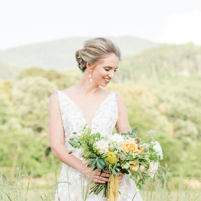 Bride in a white gown smiles gently, holding a lush bouquet of yellow and white flowers