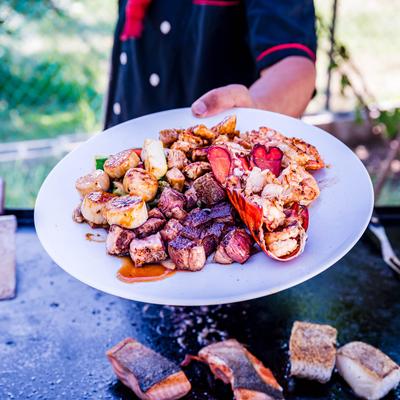 Chef holding a plate of assorted grilled meats and seafood.
