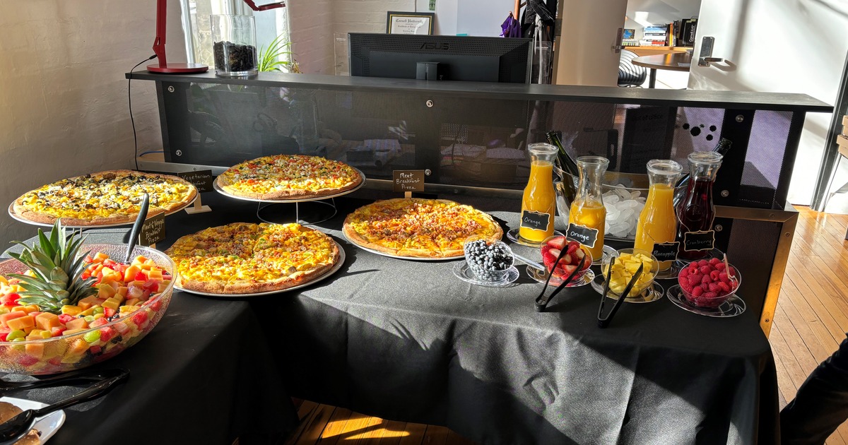 Buffet table with various pizzas, fresh juices and fruit bowls