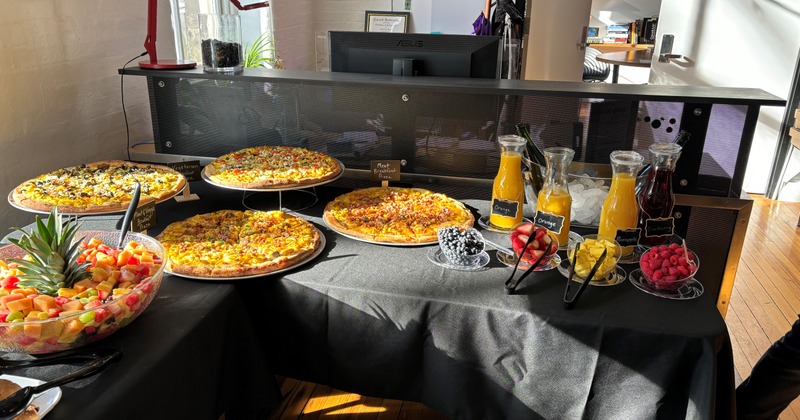 Buffet table with various pizzas, fresh juices and fruit bowls