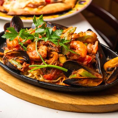 Seafood pasta on a hotplate with muscles and a piece of parsley on top..