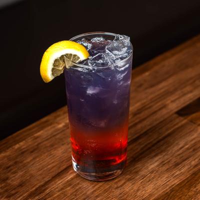 Red and purple layered cocktail served in a highball glass with a lemon slice garnish.