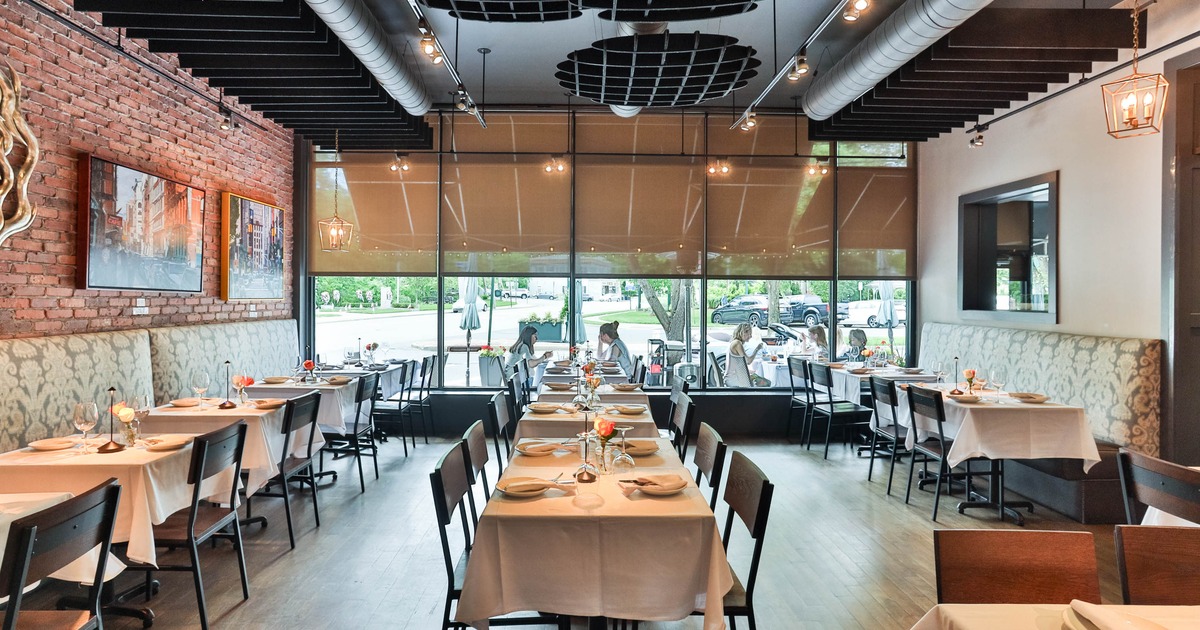 Interior of a modern restaurant with wooden floors, brick walls, and tables with white tablecloths