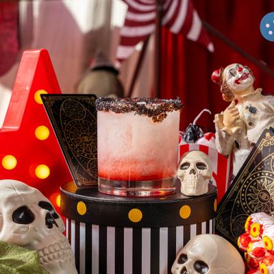 Bloody Tequila Sunset cocktail on a black-and-white striped stand, alongside spooky props.