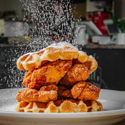 Fried chicken and waffles on a plate, being dusted with powdered sugar.