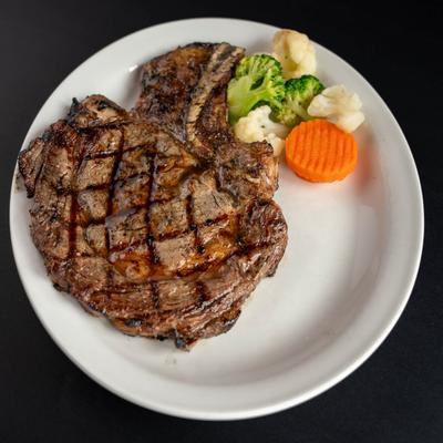 Grilled ribeye steak served with steamed broccoli, cauliflower, and a slice of carrot.