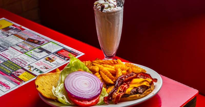 Bacon cheeseburger with fries and Oreo milkshake on a red table