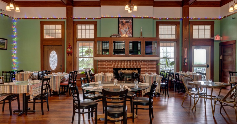 Interior of a restaurant featuring round tables with striped tablecloths, black wooden chairs