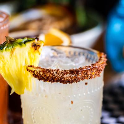 Cocktail in chili-rimmed glass, garnished with a slice of pineapple, close-up.