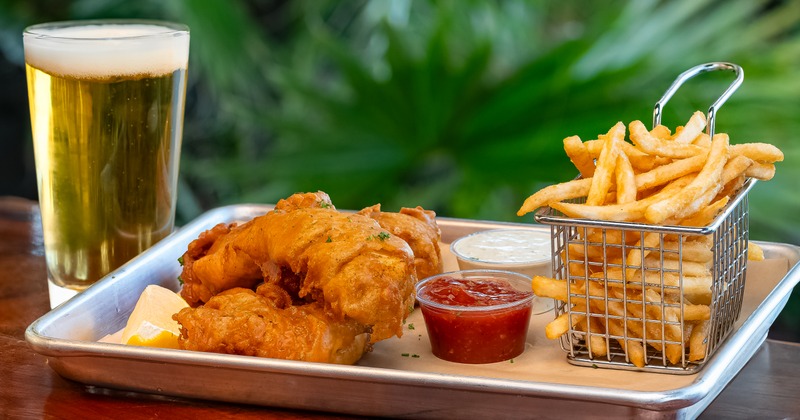 Fish and chips with sauces on a tray,  paired with a glass of beer