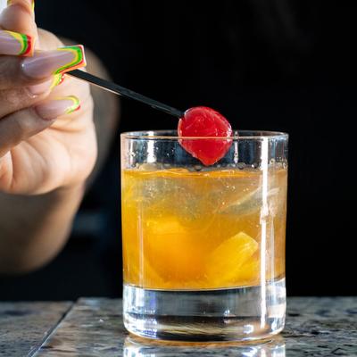 A person enjoying an orange cocktail with cherry decoration.