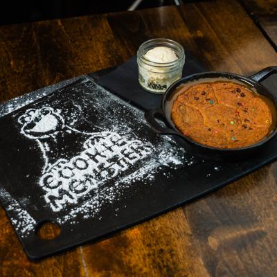 Skillet cookie & ice cream served on a black  board with Cookie Monster powdered sugar art.