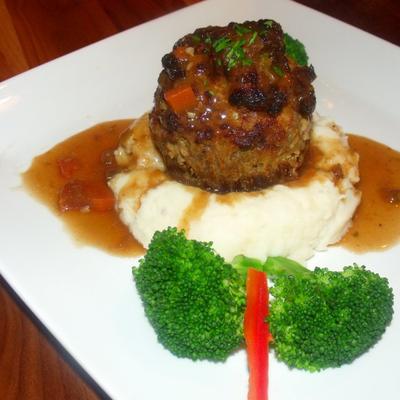 A meatball served over mashed potatoes with broccoli garnish.