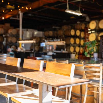 Sunlit tables and chairs, stacked barrels in the background.