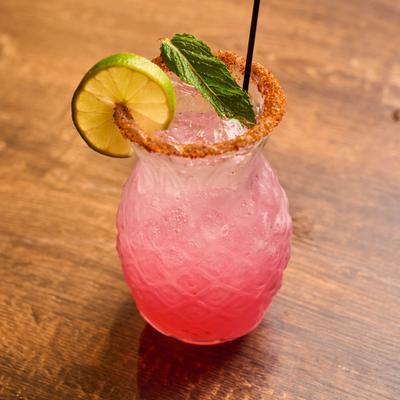 Pink cocktail with mint and lime garnish served in a pineapple-shaped glass.
