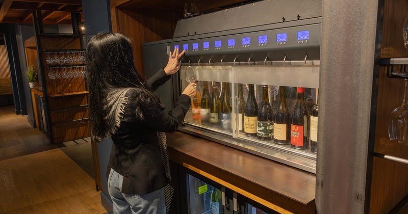 A person dispenses wine from a sleek, glass-fronted wine machine