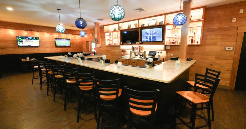 A cozy bar with wooden paneling, a marble bar counter and blue hanging lights.