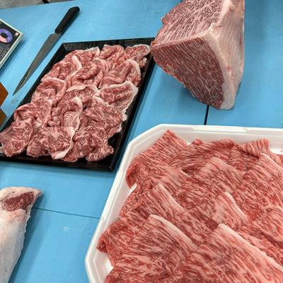 Sliced marbled beef is arranged on trays on a blue table, large beef chunk is placed nearby.