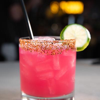 A rimmed glass of pink cocktail with lime wheel cocktail garnish.