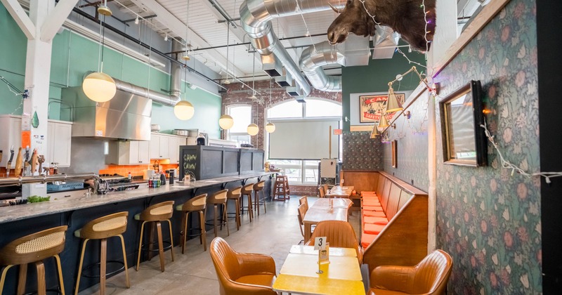 Interior of a café with a long counter, wooden stools, floral wallpaper, and orange booth seating