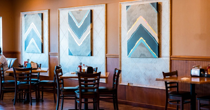 Interior, seating area, tables for four, abstract paintings on the wall, condiments on the tables