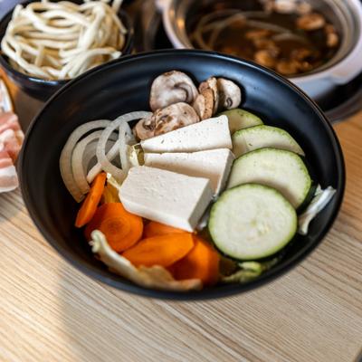 Tofu and vegetables bowl along with broth pot and noodles cup.