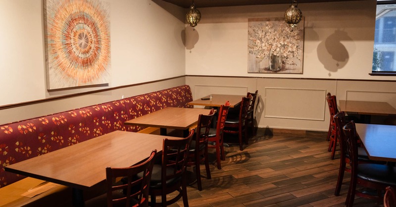 Restaurant interior with wooden tables, red floral-patterned bench, hanging lights