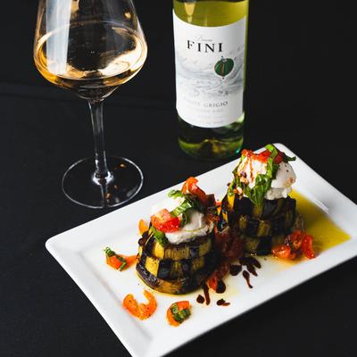 Grilled vegetable stacks topped with burrata and cherry tomatoes, served with white wine.