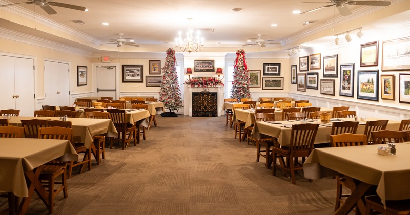 Spacious dining area with dining tables set for guests and two Christmas trees by the fireplace