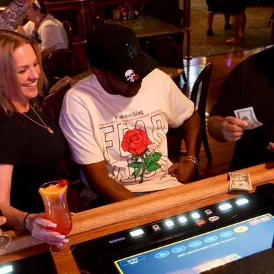 Individuals interacting with a gaming machine while seated at a bar counter.