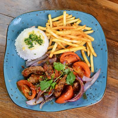 A plate of steak strips with tomatoes, onions, rice, and fries.