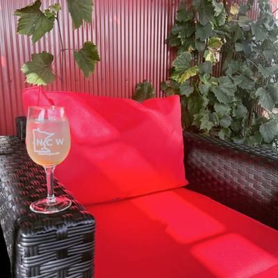 Wicker chair with vibrant red cushions, lush green vines on a wall, and a glass of white wine.