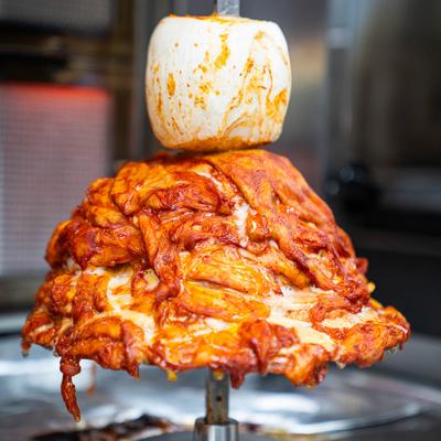 Marinated pork being cooked on a vertical rotisserie spit.