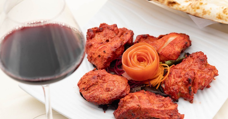 Chicken tikka served with a carrot rose flower and a glass of red wine