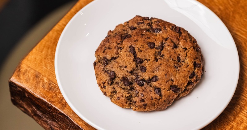 Two chocolate chip cookies on a white plate atop a rustic wooden table