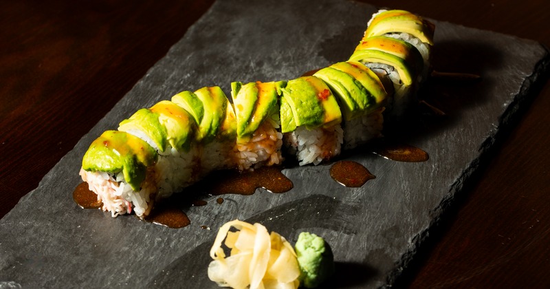 Avocado sushi roll arranged on slate with pickled ginger and wasabi