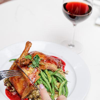 Roasted duck leg with green beans, rice, red sauce, and a glass of red wine