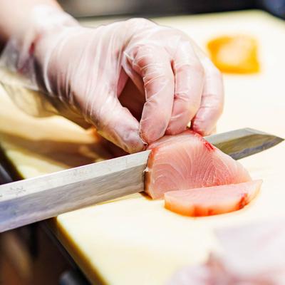 Chef slices raw fish with a sharp knife on a cutting board.