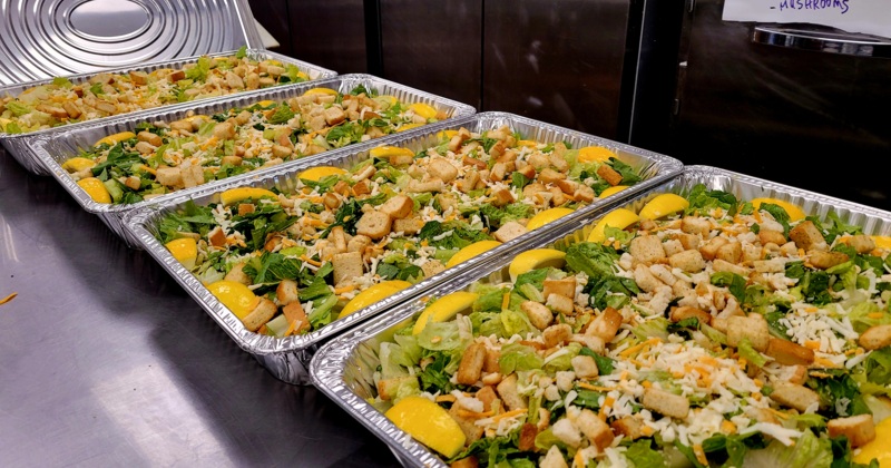 Several large catering trays of Caesar salad