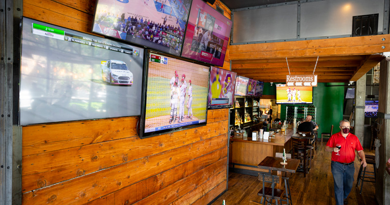 Restaurant interior - the wall with 5 flat screen TVs, a member of the staff wearing a mask on his way to serve the customers